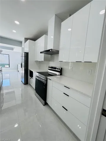 Kitchen with white cabinets, wall chimney range hood, stainless steel appliances, and tasteful backsplash