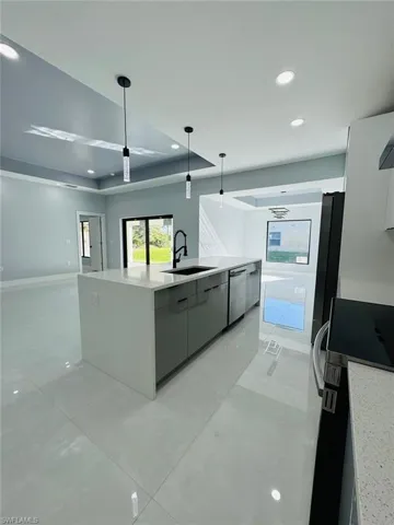 Kitchen featuring stove, sink, a center island with sink, dishwasher, and hanging light fixtures