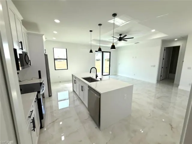 Kitchen with white cabinets, light marble finish flooring, stainless steel appliances, a kitchen island with sink, and light stone countertops