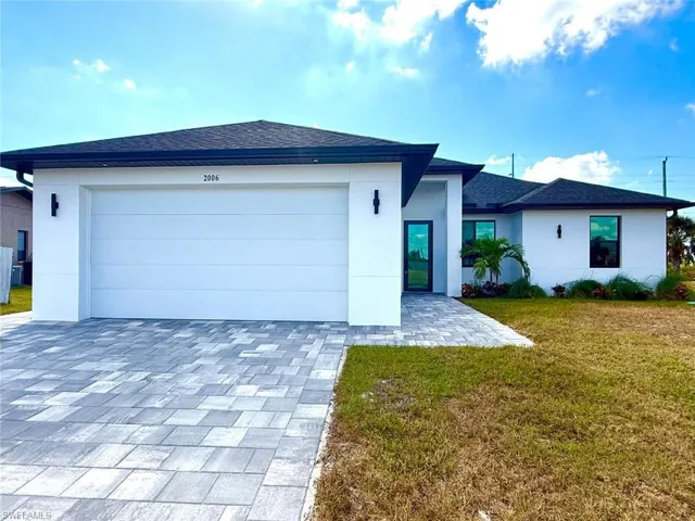 View of front facade with a front yard, a shingled roof, decorative driveway, and stucco siding