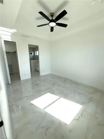 Unfurnished bedroom with ensuite bath, ceiling fan, and marble finish floors