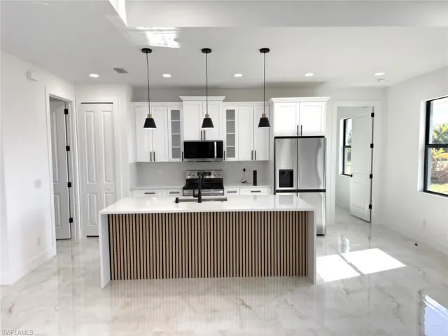 Kitchen featuring stainless steel appliances, light stone counters, a center island with sink, white cabinets, and recessed lighting