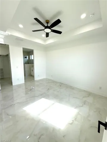 Unfurnished bedroom with a tray ceiling, recessed lighting, ceiling fan, ensuite bath, and light marble finish flooring