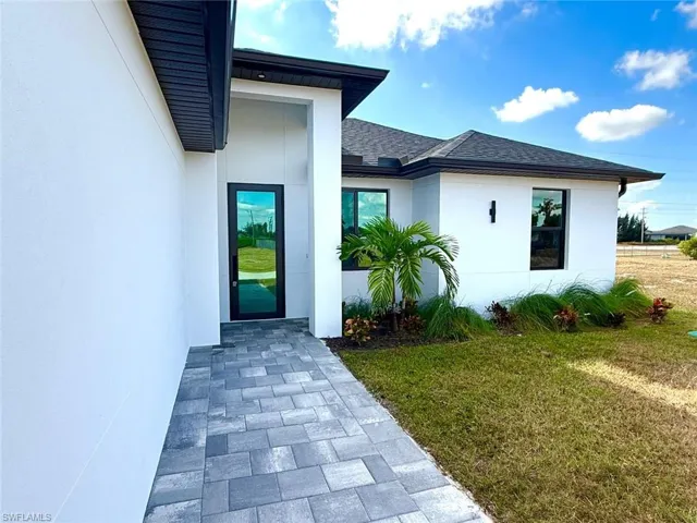 Property entrance with a lawn, stucco siding, and roof with shingles