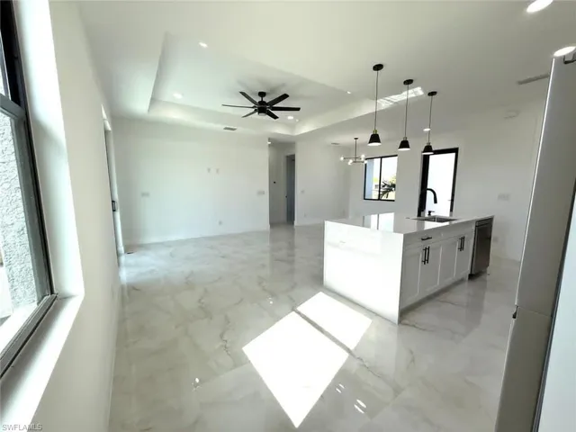 Kitchen with a tray ceiling, decorative light fixtures, white cabinets, an island with sink, and a chandelier