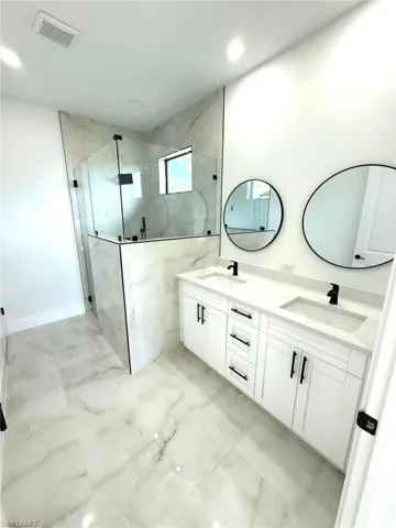 Full bath featuring light marble finish floors, double vanity, a marble finish shower, and recessed lighting