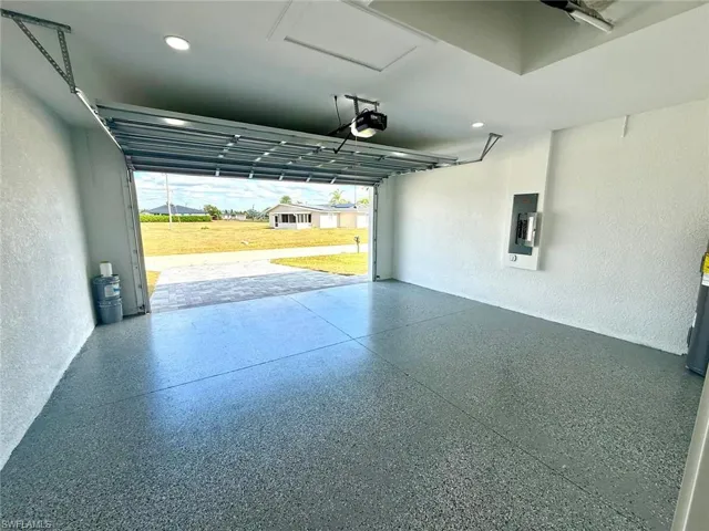 Garage featuring a textured wall, electric panel, a garage door opener, and recessed lighting
