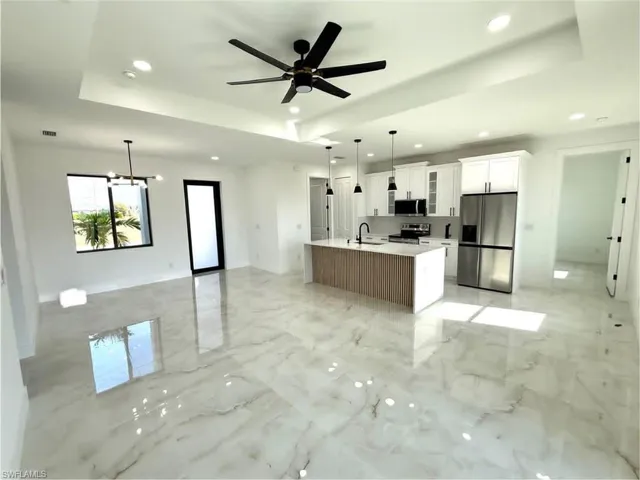 Kitchen featuring open floor plan, stainless steel appliances, white cabinets, a tray ceiling, and hanging light fixtures