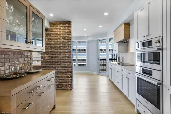 Kitchen with decorative backsplash, white cabinets, custom exhaust hood, double oven, and light hardwood / wood-style floors