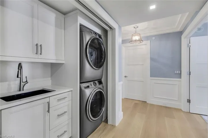Laundry room featuring sink, light wood-type flooring, and stacked washer / dryer
