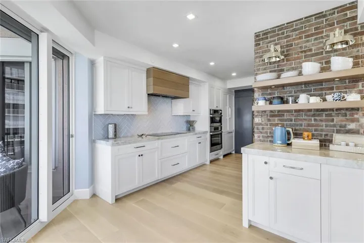Kitchen featuring light wood-type flooring, double oven, white cabinetry, premium range hood, and decorative backsplash
