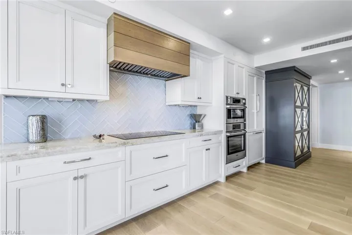 Kitchen featuring stainless steel double oven, white cabinetry, light hardwood / wood-style floors, backsplash, and premium range hood