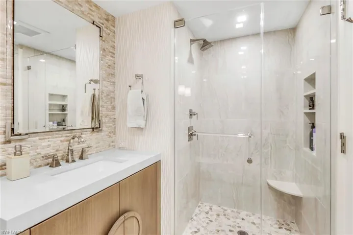 Bathroom featuring a shower with shower door, vanity, and decorative backsplash