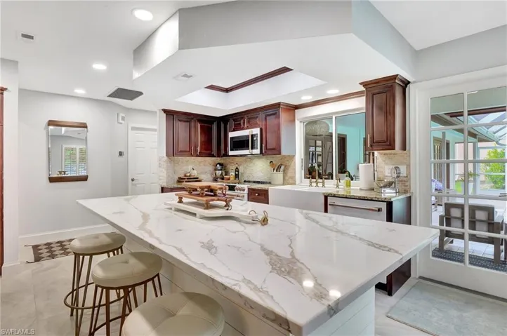 Kitchen with a kitchen breakfast bar, light stone countertops, appliances with stainless steel finishes, tasteful backsplash, and light tile patterned flooring