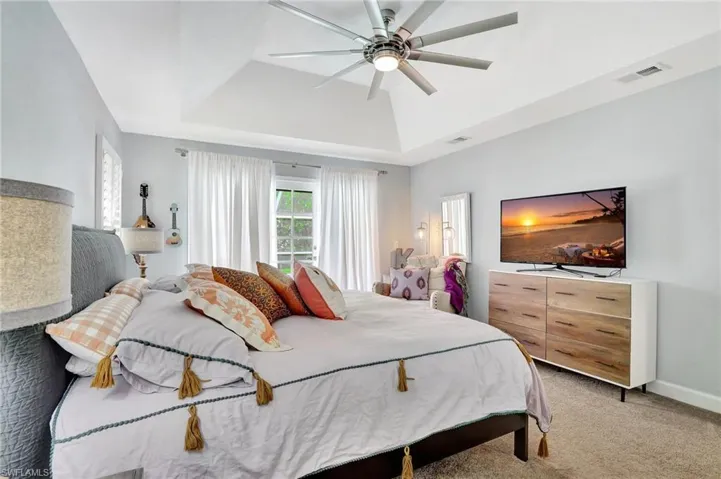 Carpeted bedroom with a raised ceiling and ceiling fan