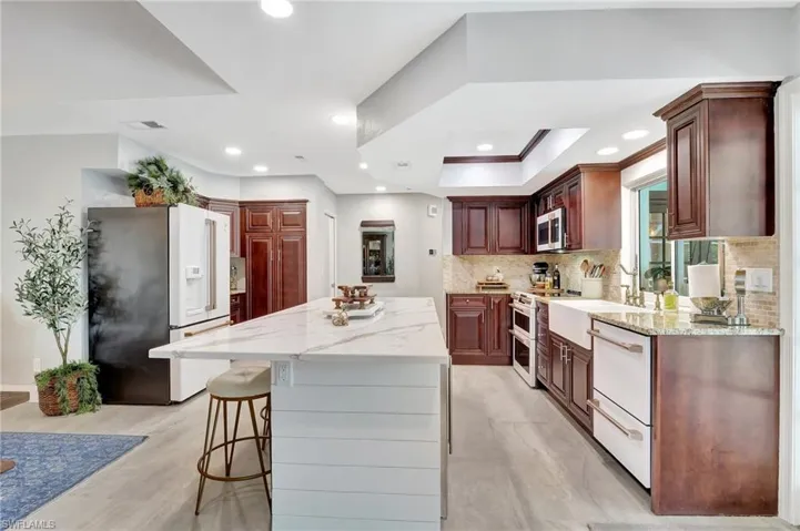 Kitchen with backsplash, light stone countertops, stainless steel appliances, a kitchen breakfast bar, and a kitchen island