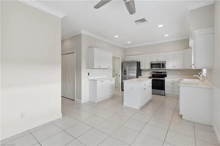 Kitchen with appliances with stainless steel finishes, crown molding, a ceiling fan, light countertops, and light tile patterned flooring