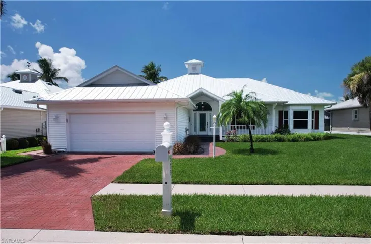 Ranch-style home with decorative driveway, an attached garage, a front lawn, and a metal roof
