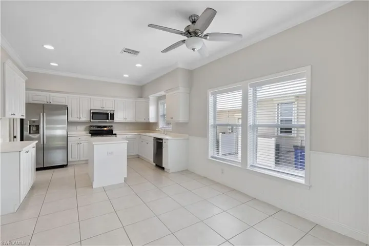 Spacious, open kitchen with stainless steel appliances, ornamental molding, a kitchen island, light countertops, and a ceiling fan