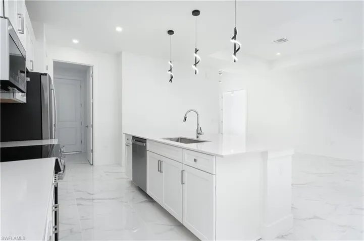 Kitchen with hanging light fixtures, white cabinetry, a kitchen island with sink, stainless steel appliances, and light stone countertops