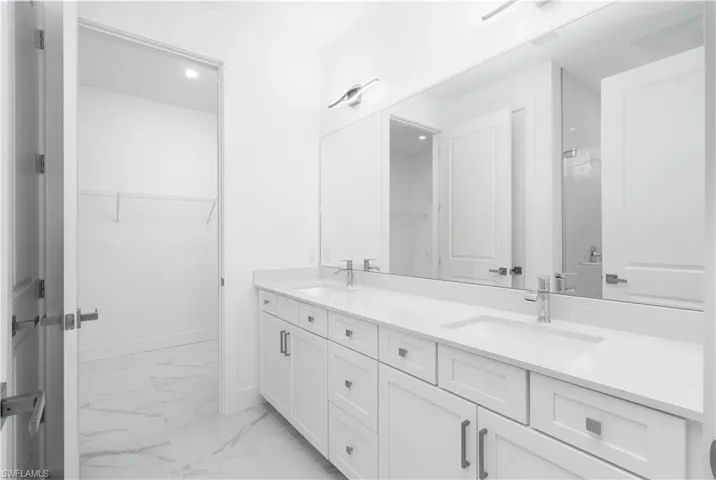 Bathroom featuring double vanity, a spacious closet, and light marble finish floors