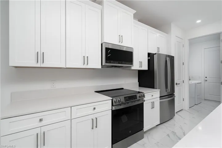 Kitchen with stainless steel appliances, white cabinetry, light marble finish flooring, washer and clothes dryer, and recessed lighting