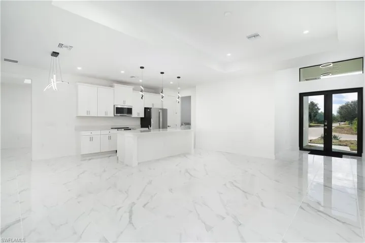 Kitchen with open floor plan, white cabinetry, stainless steel appliances, a center island with sink, and decorative light fixtures