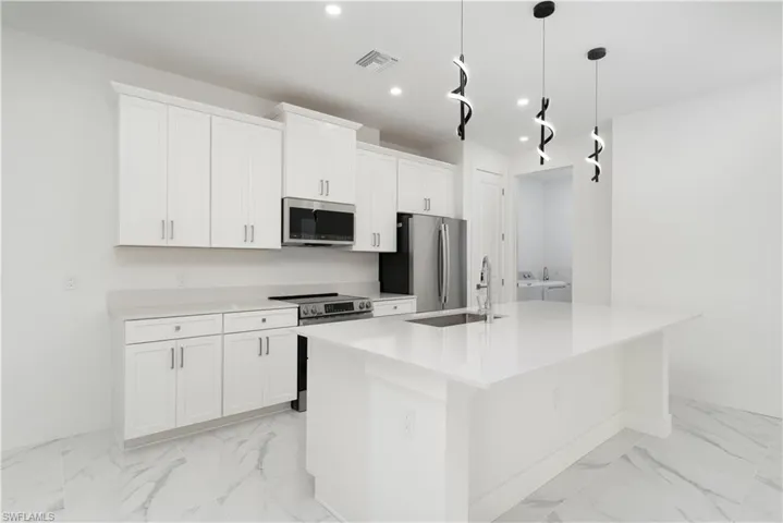 Kitchen featuring stainless steel appliances, independent washer and dryer, white cabinetry, a kitchen island with sink, and pendant lighting
