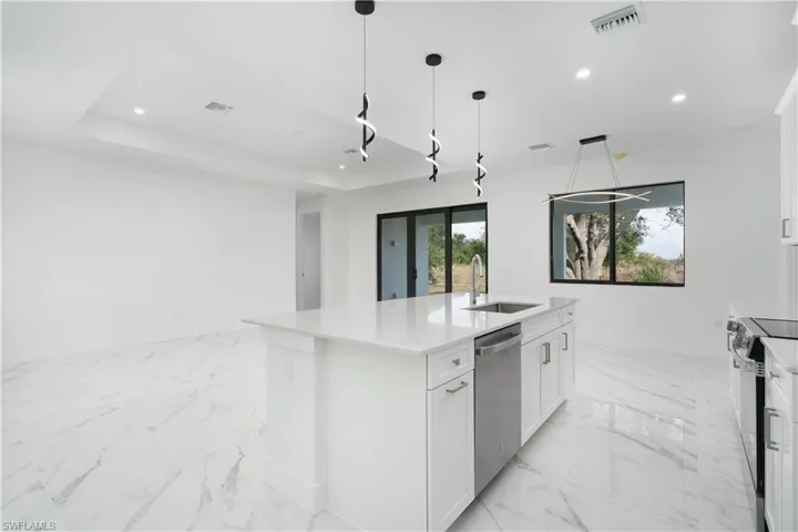 Kitchen with white cabinetry, a center island with sink, hanging light fixtures, light stone counters, and dishwasher