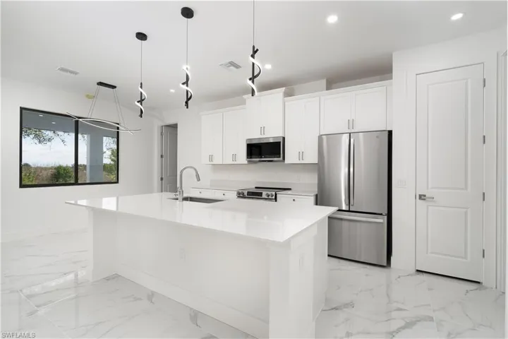 Kitchen with stainless steel appliances, white cabinets, an island with sink, decorative light fixtures, and light stone counters