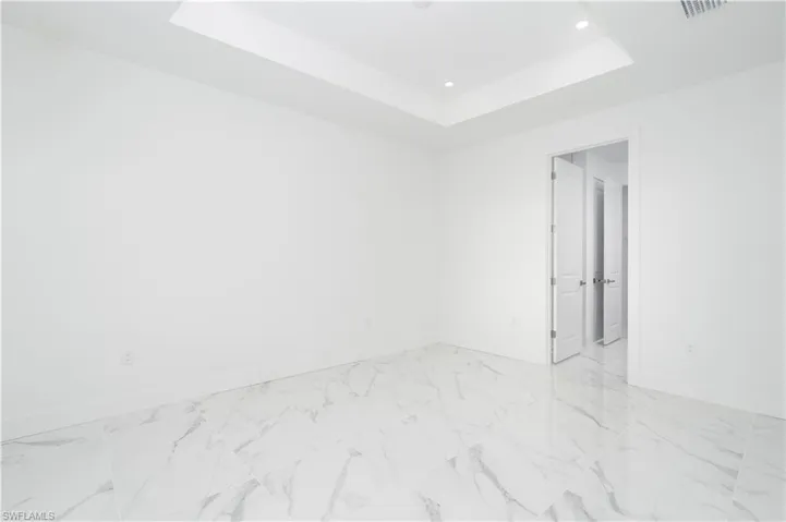 Spare room featuring a raised ceiling, light marble finish flooring, and recessed lighting