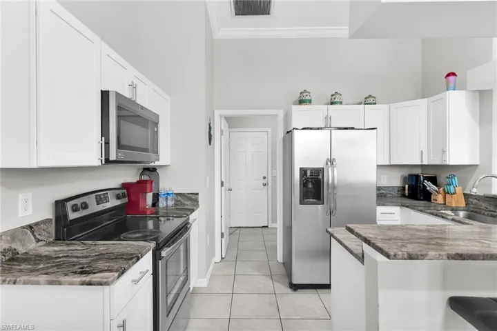 Kitchen featuring stainless steel appliances, white cabinetry, a peninsula, light tile patterned floors, and crown molding