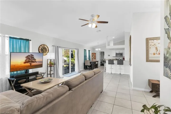 Living room with light tile patterned floors, ceiling fan, lofted ceiling, and ornamental molding