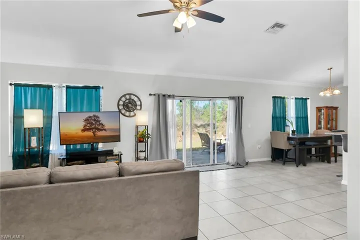 Living area with a ceiling fan, light tile patterned flooring, crown molding, and hanging lights