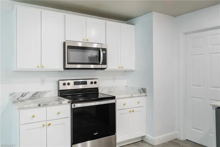 Kitchen with stainless steel appliances, white cabinets, and light stone countertops