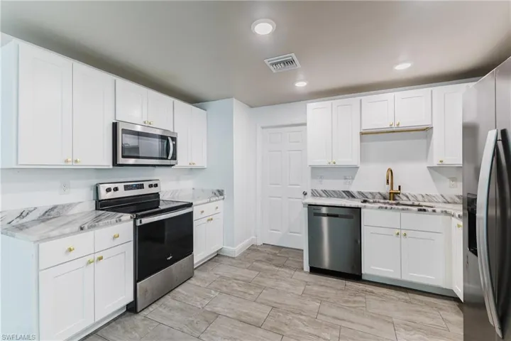 Kitchen featuring stainless steel appliances, white cabinetry, recessed lighting, light stone counters, and wood tiled floors
