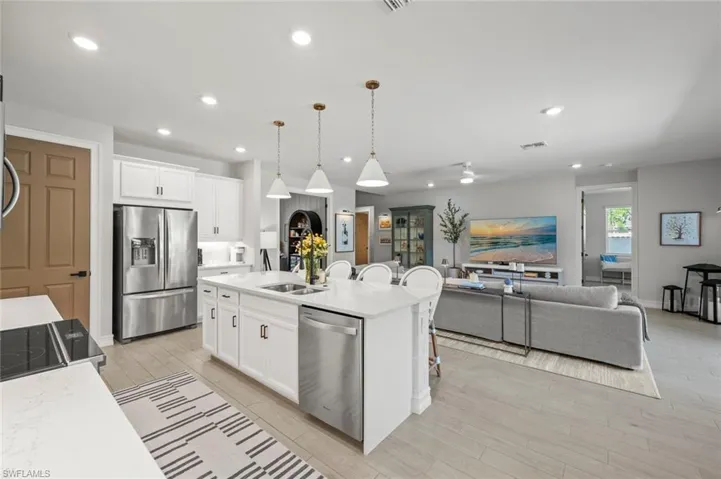 Kitchen featuring decorative light fixtures, stainless steel appliances, a breakfast bar, open floor plan, and white cabinetry