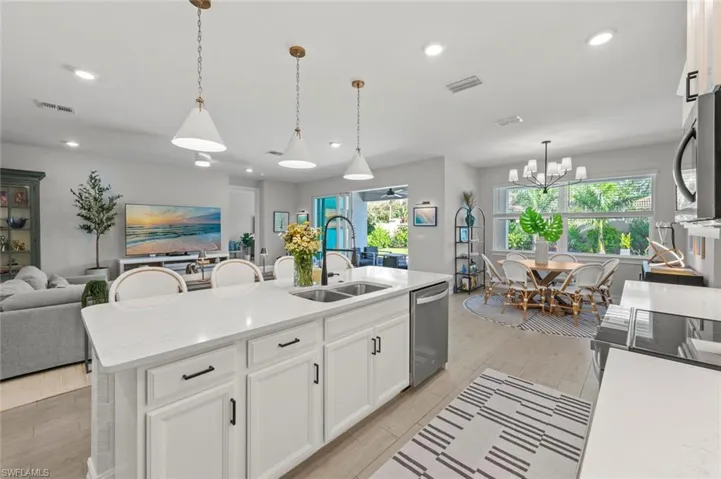 Kitchen with white cabinets, open floor plan, pendant lighting, light stone countertops, and stainless steel appliances
