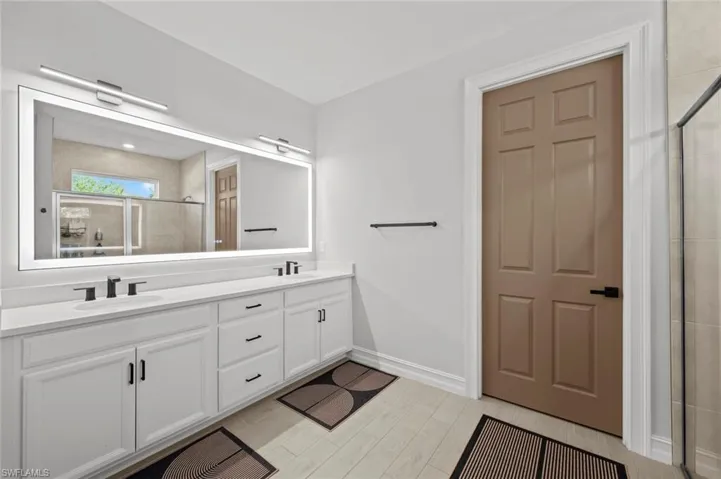 Full bathroom featuring a shower stall, double vanity, and wood tiled floors