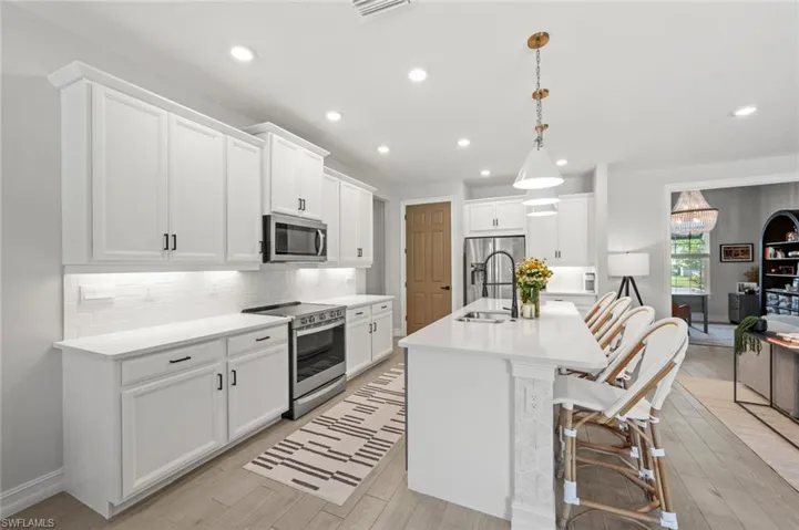 Kitchen with appliances with stainless steel finishes, a breakfast bar area, pendant lighting, white cabinets, and tasteful backsplash
