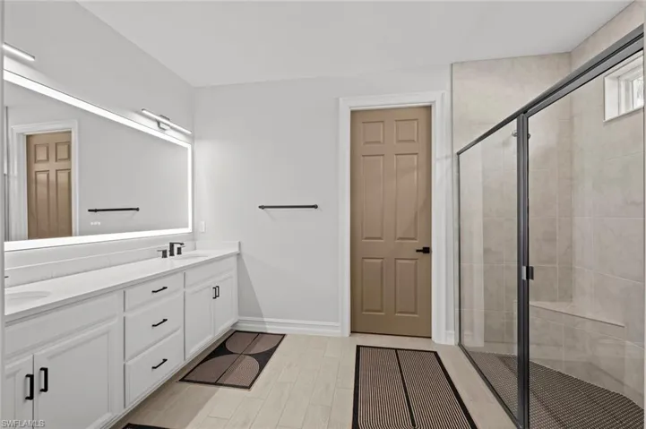 Full bath featuring a stall shower, double vanity, and wood finish floors