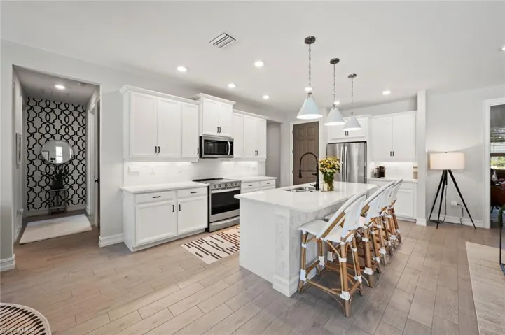 Kitchen with a kitchen breakfast bar, appliances with stainless steel finishes, decorative light fixtures, a center island with sink, and white cabinets