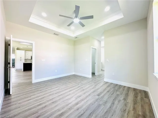 Empty room featuring crown molding, light wood-type flooring, recessed lighting, a ceiling fan, and a tray ceiling