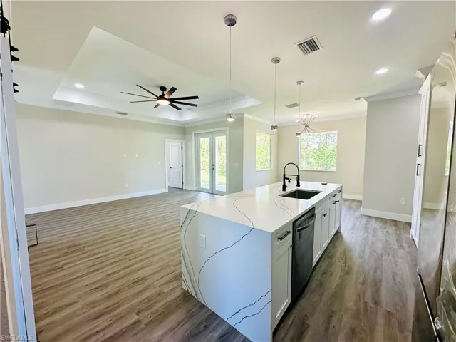 Kitchen with white cabinets, pendant lighting, open floor plan, light stone counters, and crown molding