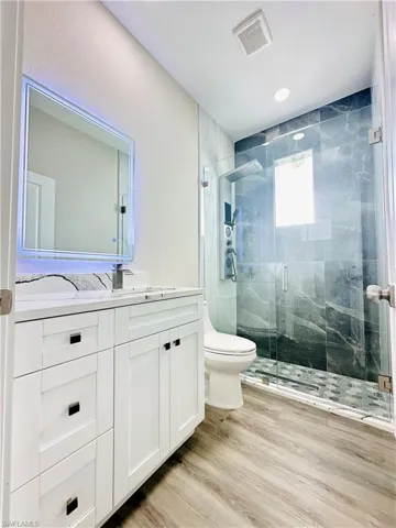 Bathroom with vanity, a marble finish shower, and light wood-style floors
