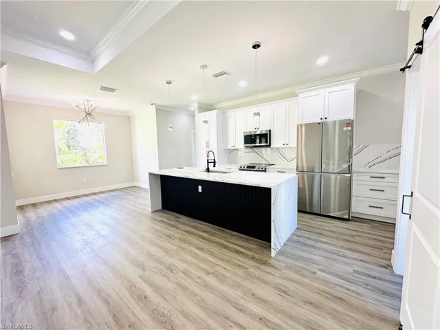 Kitchen featuring appliances with stainless steel finishes, crown molding, decorative light fixtures, white cabinetry, and light stone countertops