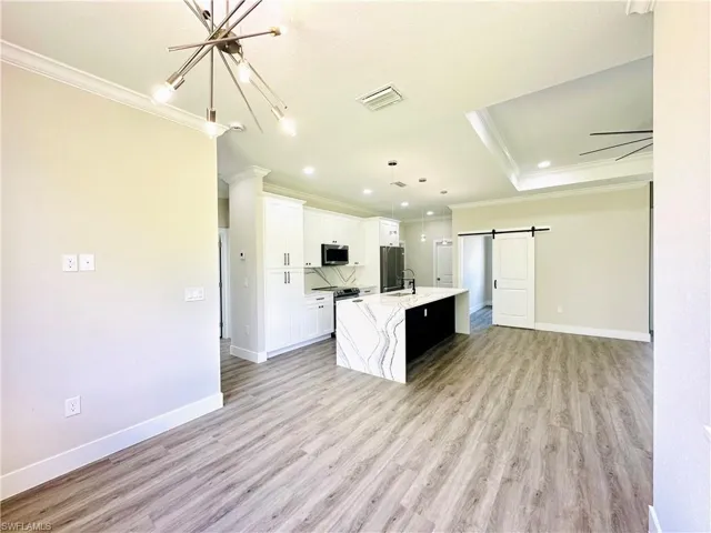 Kitchen featuring open floor plan, white cabinetry, a center island with sink, pendant lighting, and crown molding