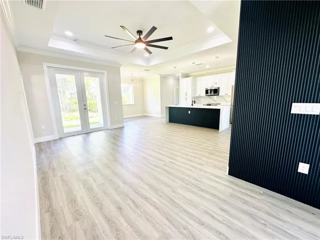 Unfurnished living room with crown molding, a raised ceiling, light wood-style flooring, a ceiling fan, and recessed lighting