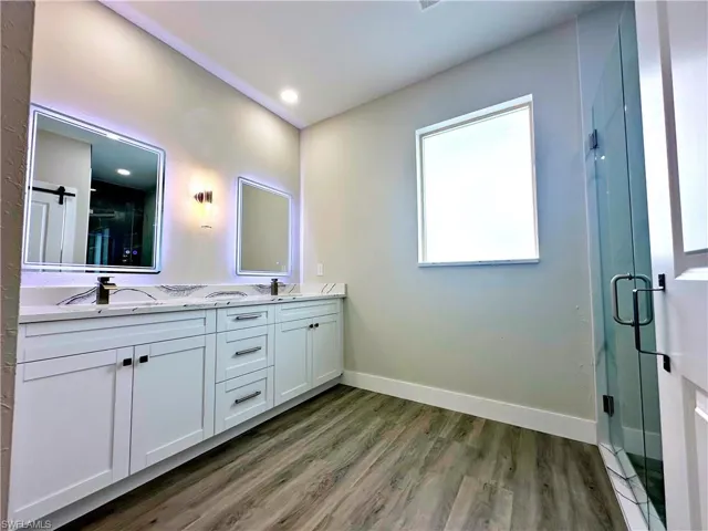 Full bath with double vanity, a stall shower, and dark wood finished floors