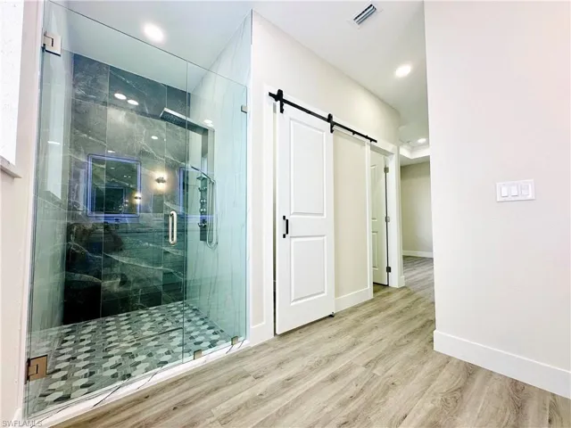 Full bath with a marble finish shower and light wood-style floors